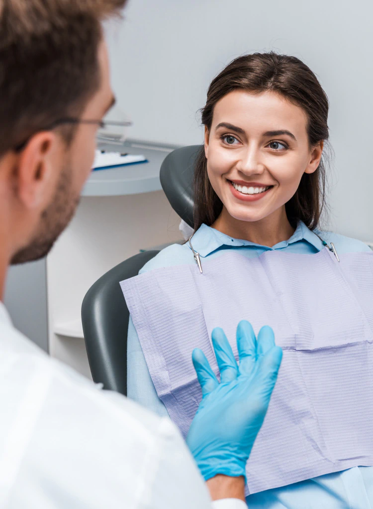 A smiling woman in a dental chair looks at a dentist who is wearing blue medical gloves.