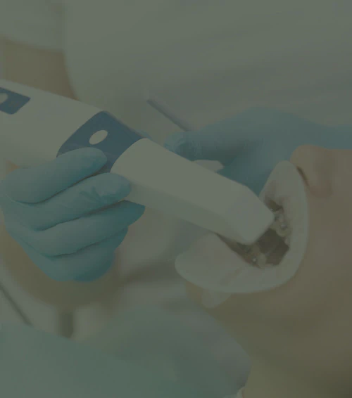 A dentist in blue gloves uses an intraoral scanner on a patient wearing a cheek retractor.