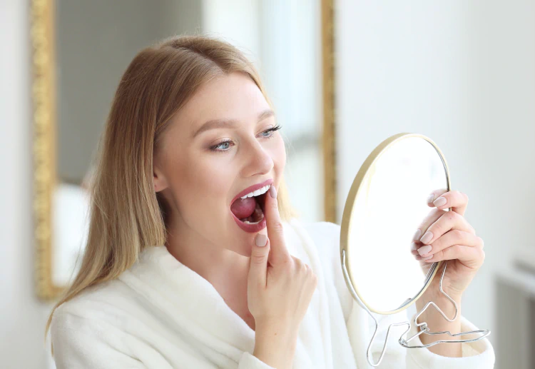 Mobile_Services_Care_for_the_Unexpected A woman in a white robe examines her teeth in a hand mirror.