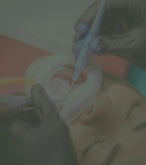 A dentist wearing black gloves performs a dental procedure on a patient whose mouth is held open with a retractor.